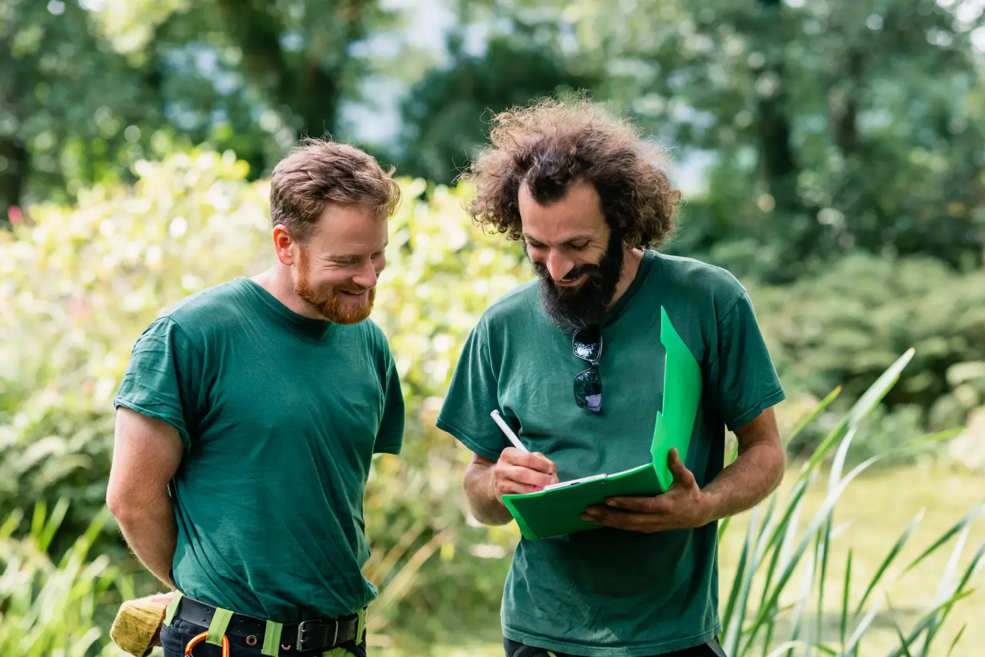 Zwei Gärtner besprechen Gartenprojekt im Grünen und notieren Details auf Klemmbrett